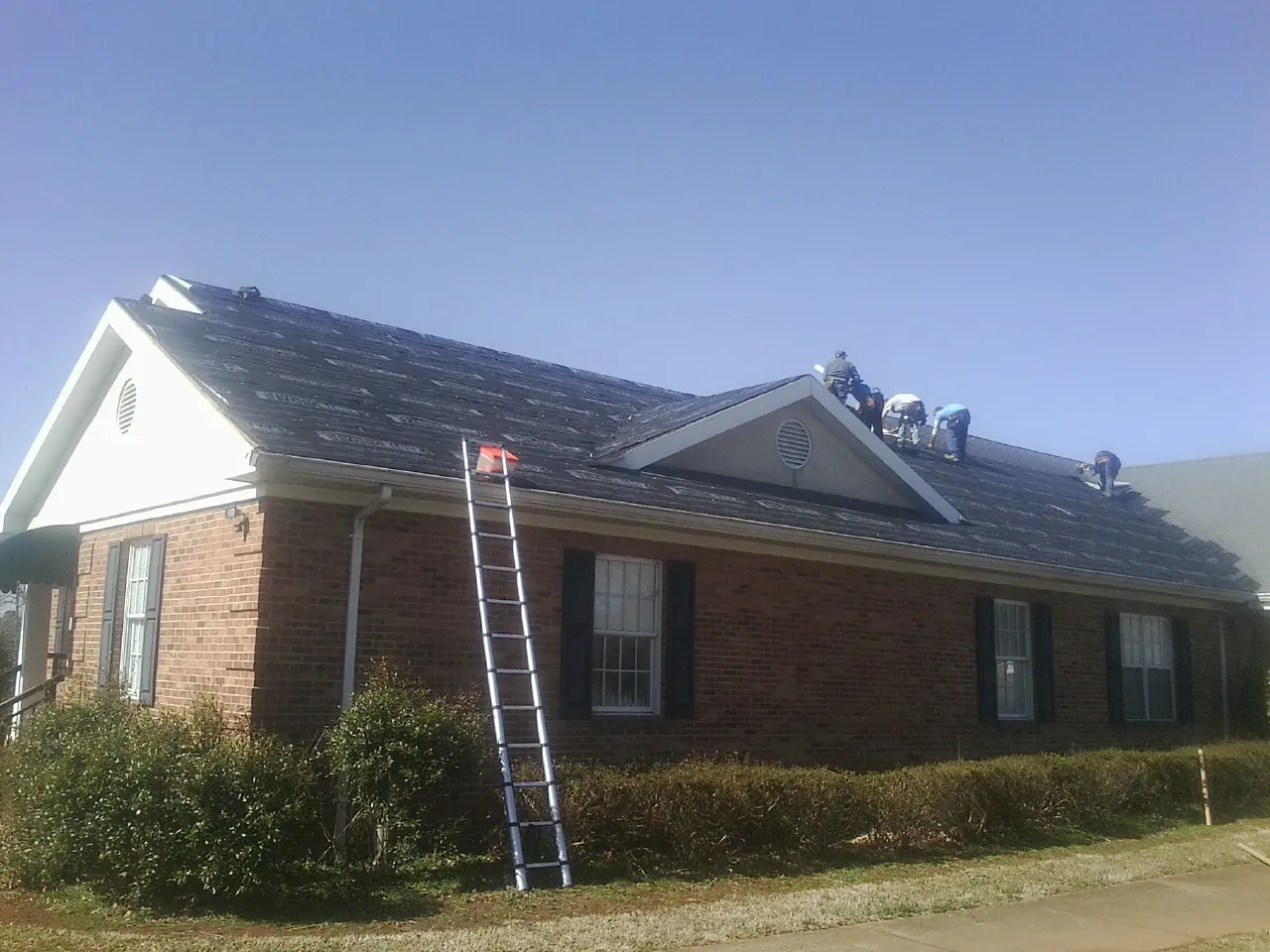 Crew tearing shingles off a brick ranch roof with a ladder set — Emergency Roof Repair work by our crew in Carthage